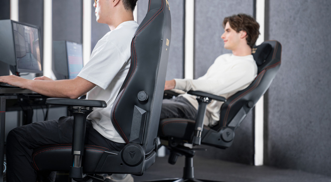 In the foreground, a man is sitting up straight at a desk. In the background, another man is leaned back comfortably